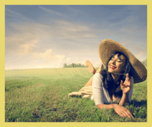 Uśmiechnięta kobieta, która ma kapelusz na głowie i leży na łące. Widać, że jest na wakacjach.
